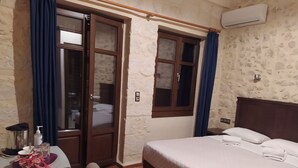 A hotel room with a bed, a wooden desk, a chair, a vase with flowers, a window with curtains, and an air conditioning unit. - Sea Front Old Town (Rethymno)