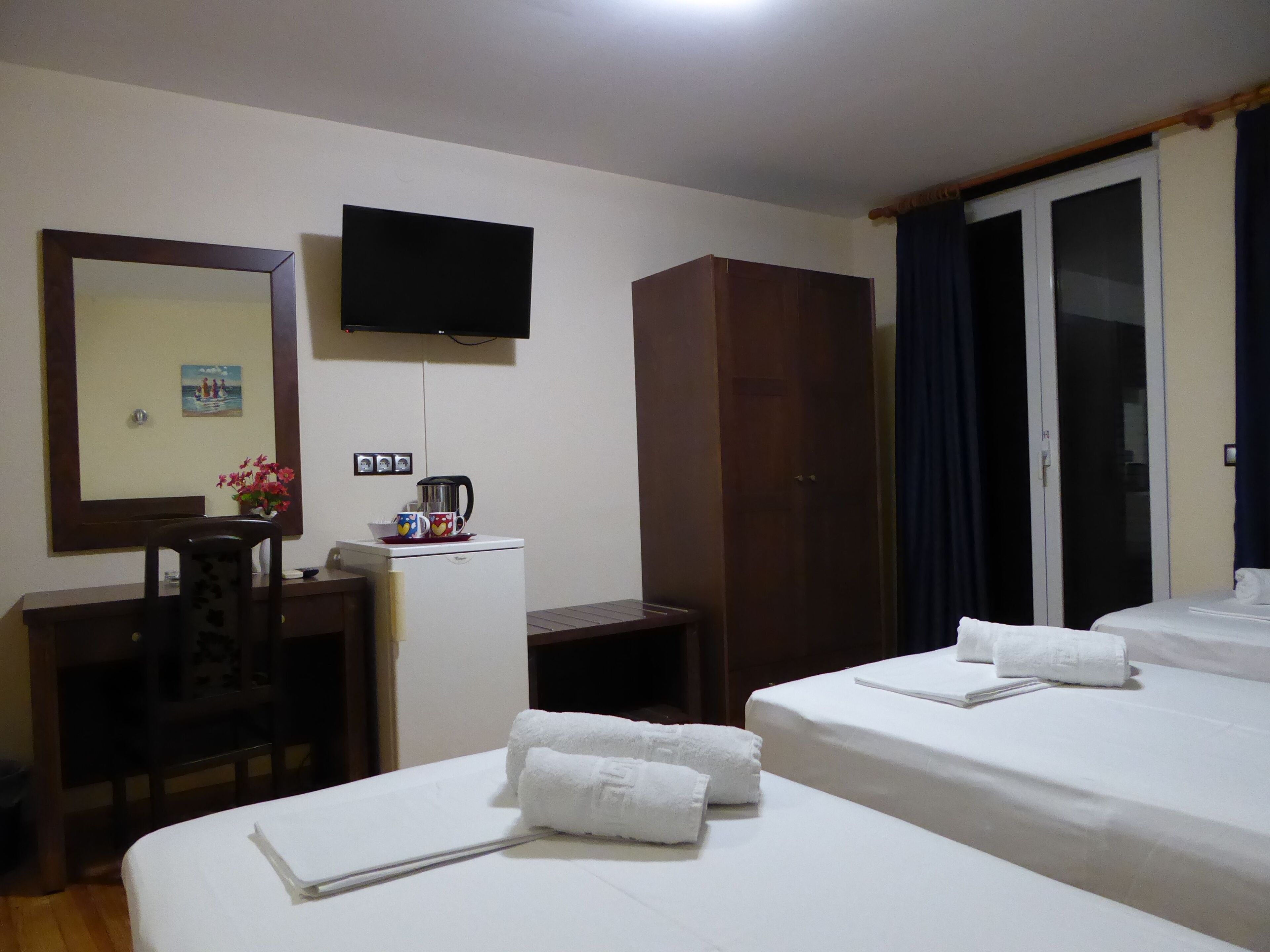 A hotel room with two beds, a TV mounted on the wall, a desk with a coffee maker, and a wardrobe.