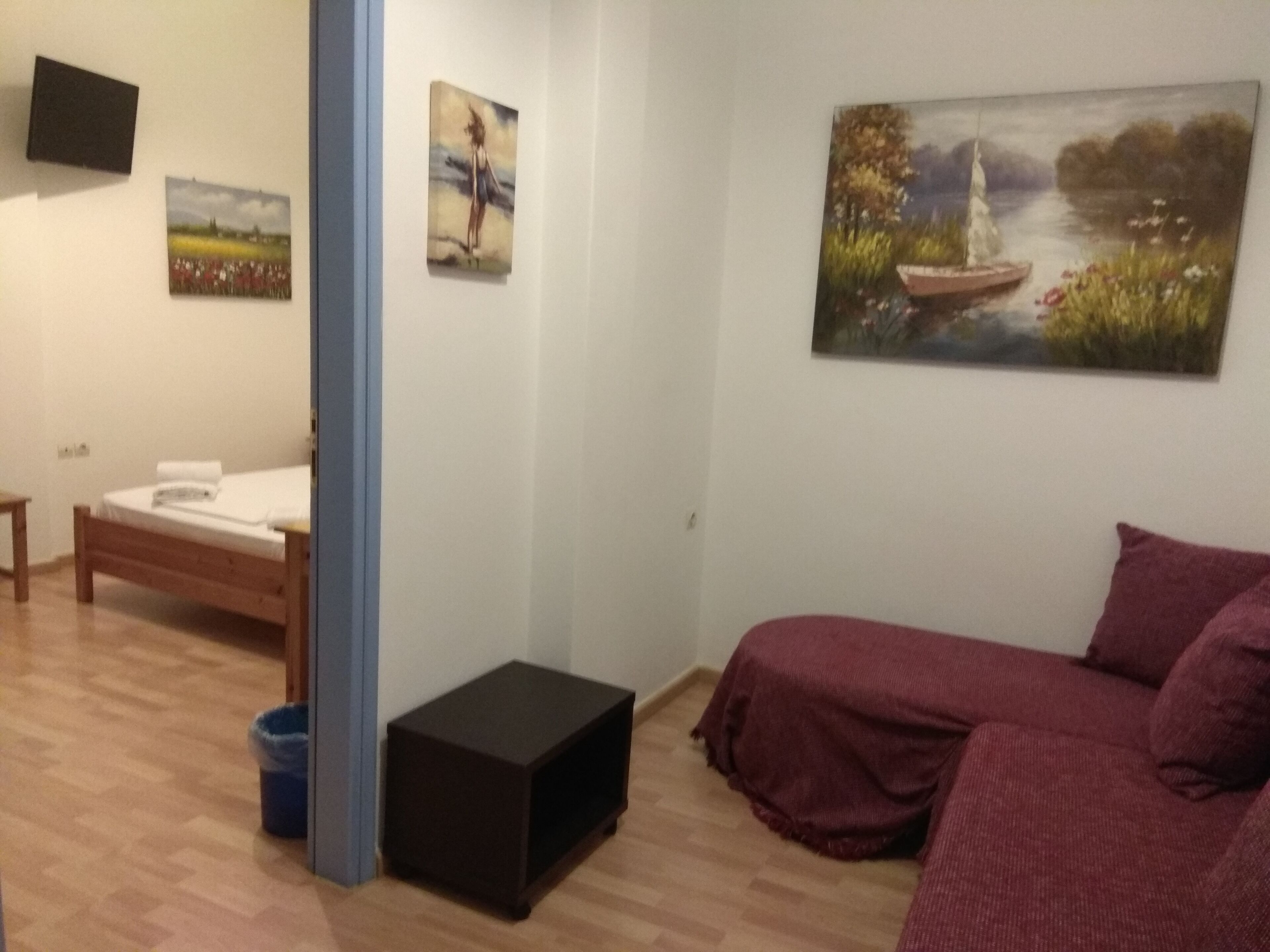 Una habitación con una cama, una mesita, un banco y un sofá. Hay cuadros en la pared.