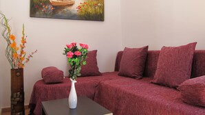 A living room with a red sofa set, a white vase with flowers, and a painting of a lake scene on the wall. - Sea Front Old Town (Rethymno)