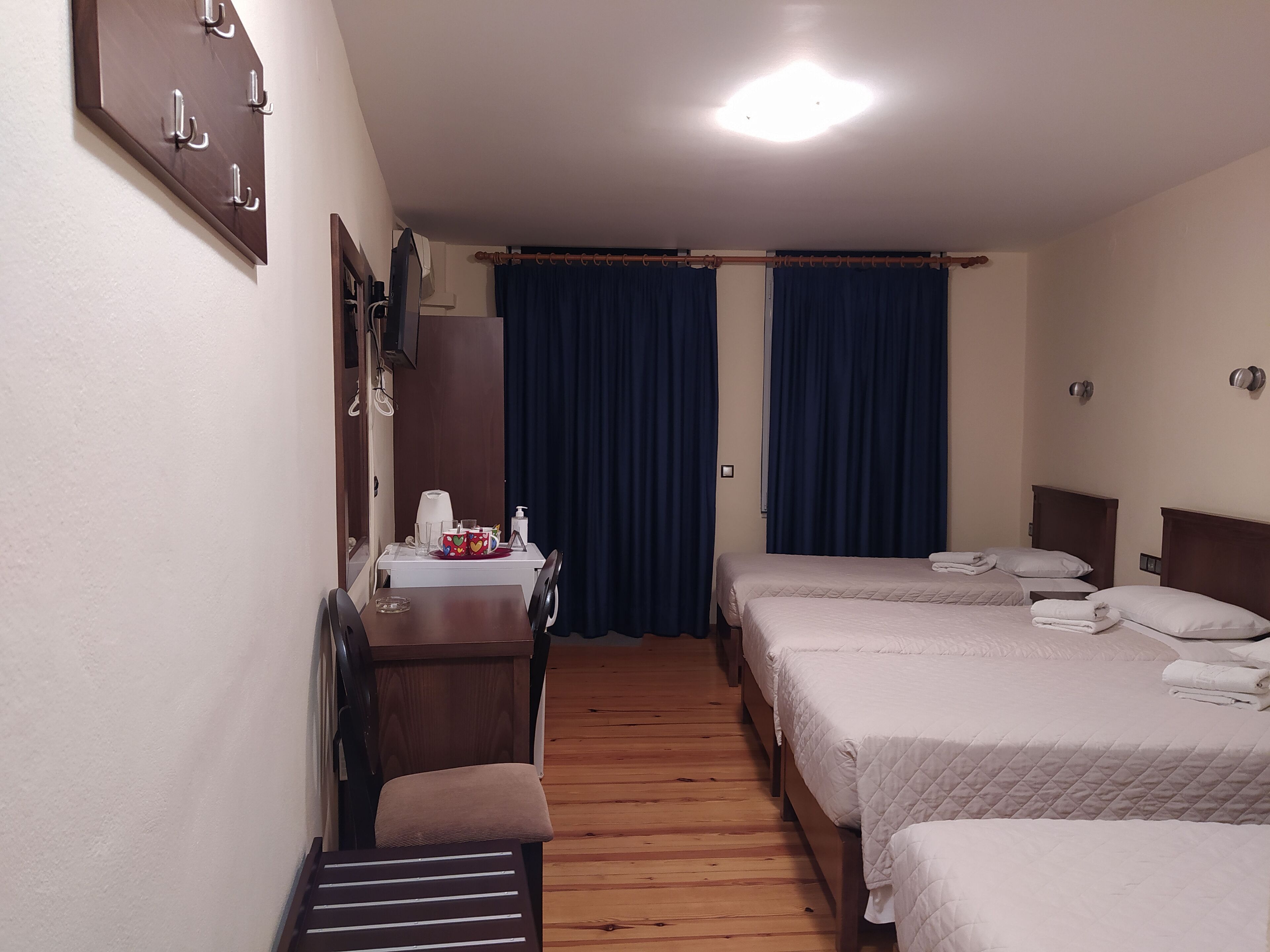 Une chambre d’hôtel avec un plancher en bois, un bureau avec une chaise, deux lits, une table de chevet avec une lampe et une fenêtre avec des rideaux.