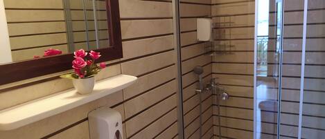 Un baño moderno con cabina de ducha de vidrio, un lavamanos blanco, un espejo y un dispensador de jabón.