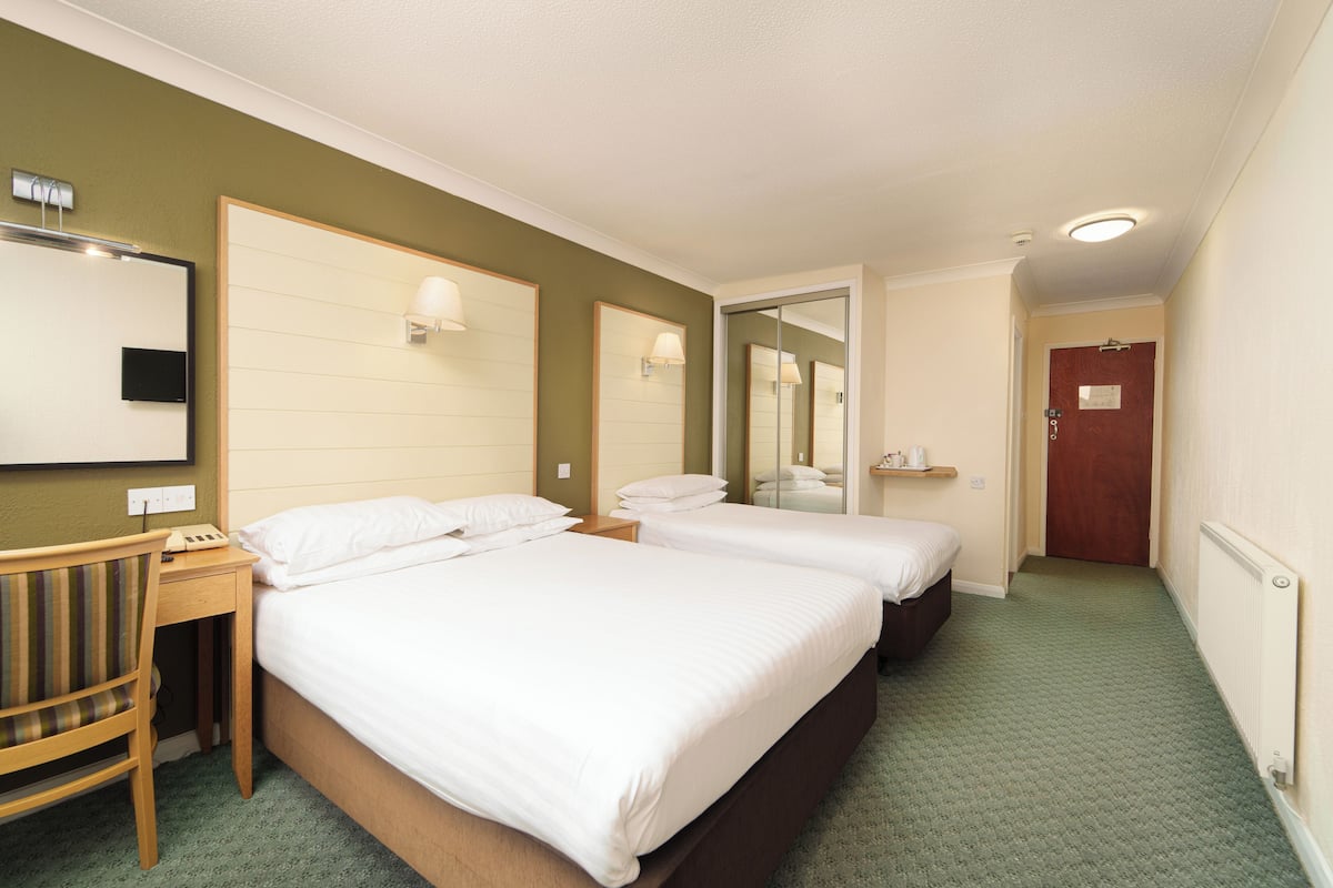 A hotel room with two beds, a desk, a chair, and a mirror.
