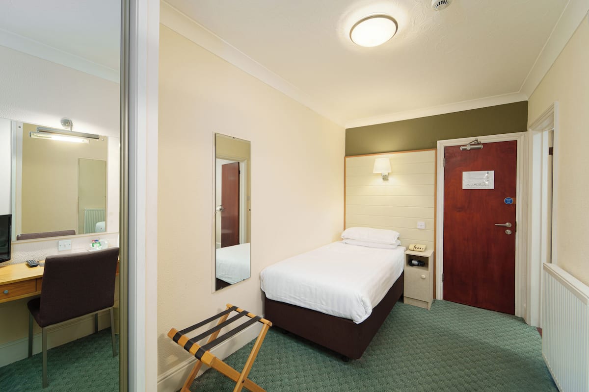 A hotel room with a bed, a desk, a chair, a mirror, a nightstand, and a door.