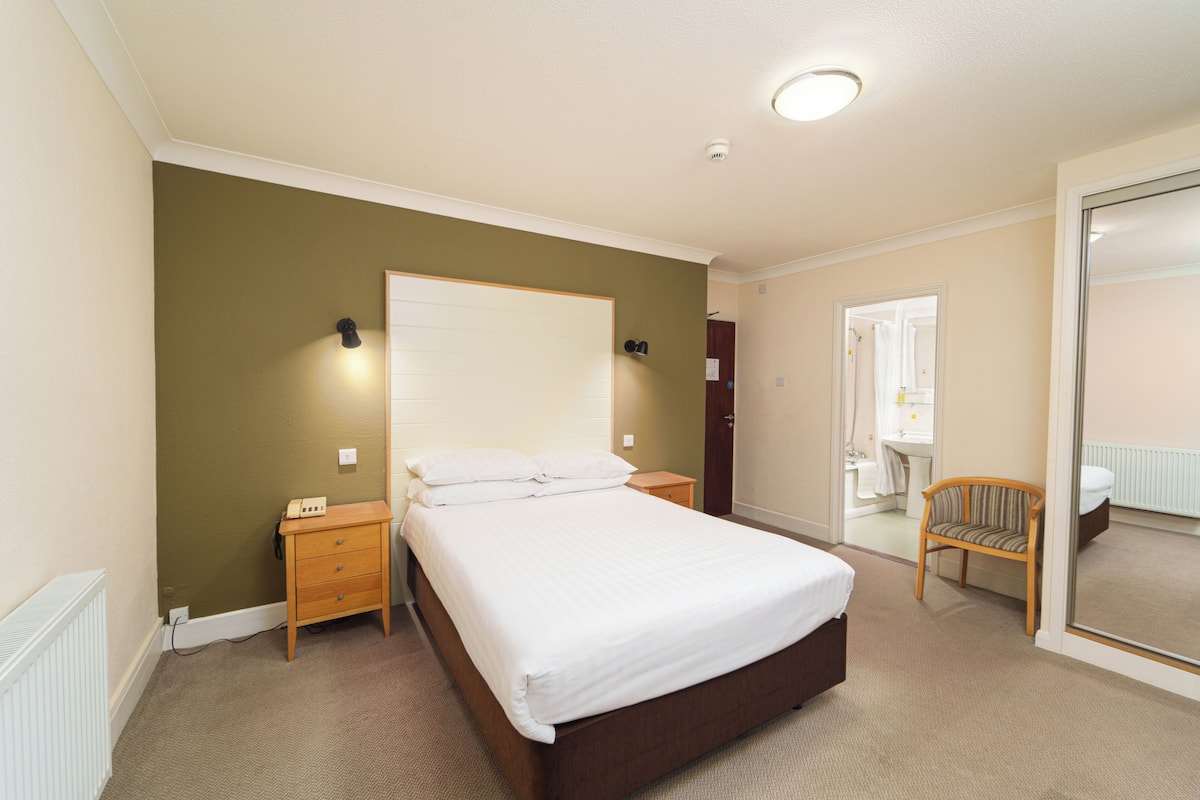 A bedroom with a large bed, a nightstand, a chair, and a bathroom visible through an open door.