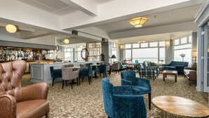 A spacious lounge area with a bar, comfortable seating, and large windows offering views. - Trouville Hotel by Compass Hospitality (Sandown)