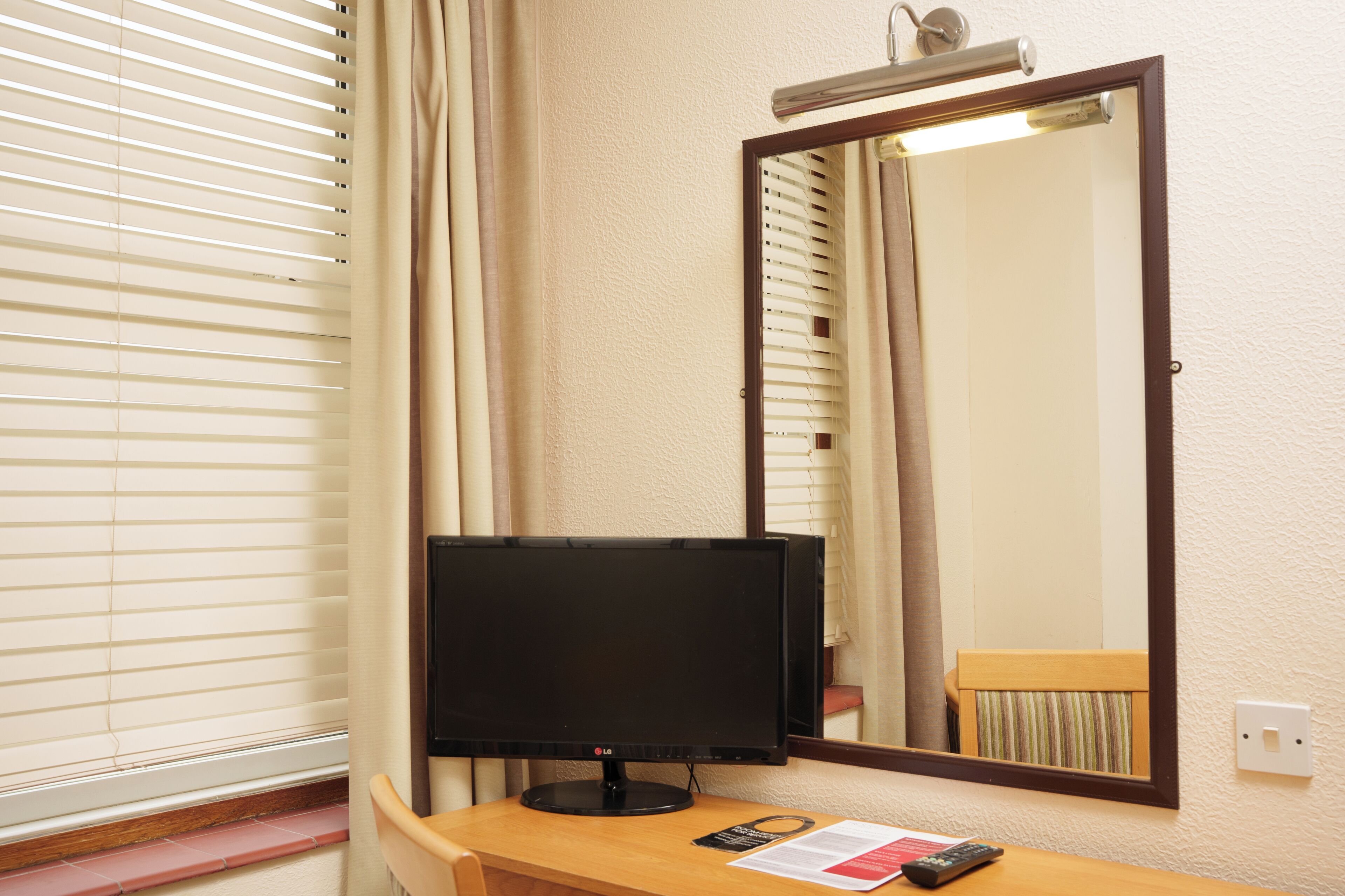 A hotel room with a flat-screen TV, a mirror, and a wooden desk.