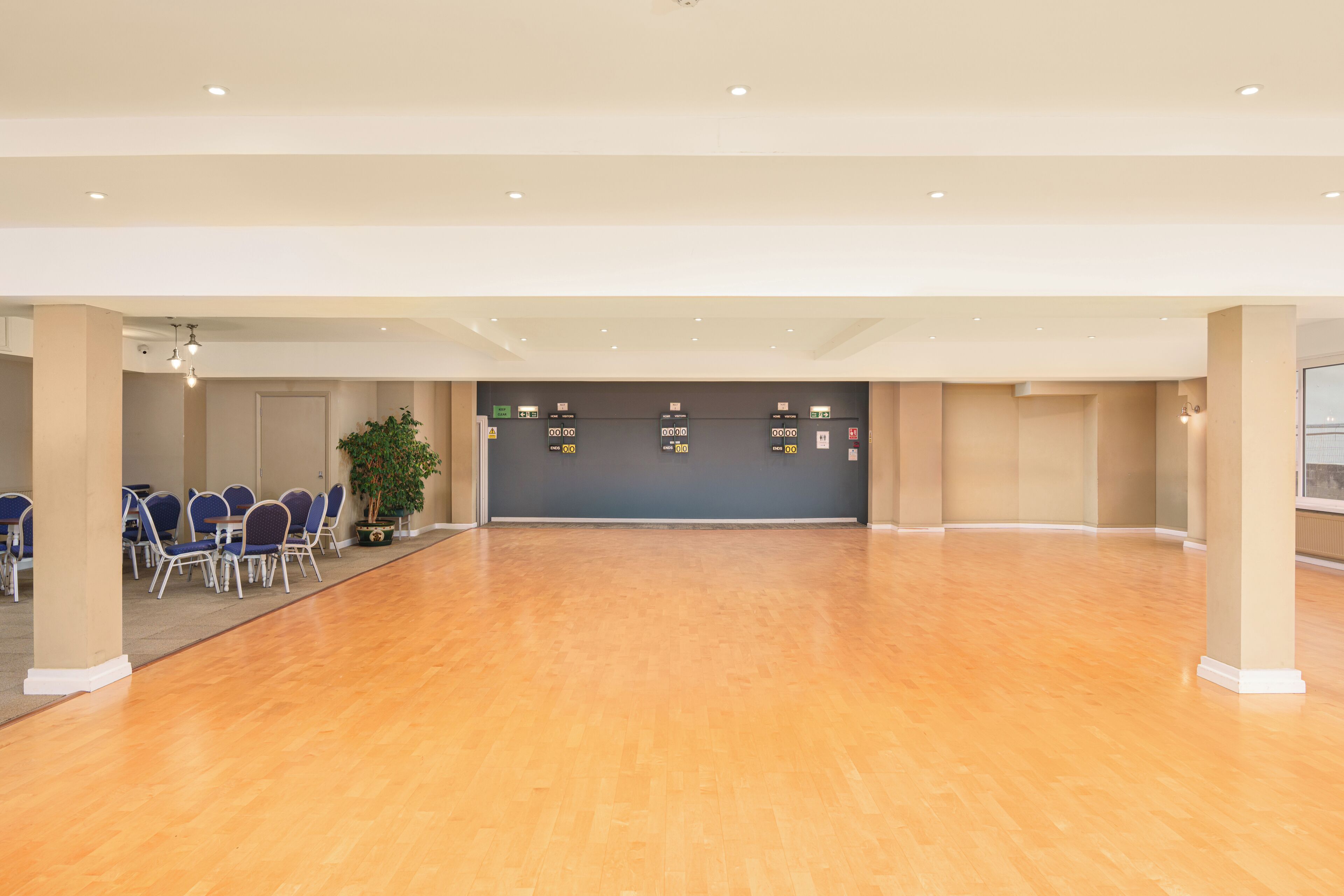 A spacious room with a wooden floor, blue chairs, and a reception desk with a grey wall.