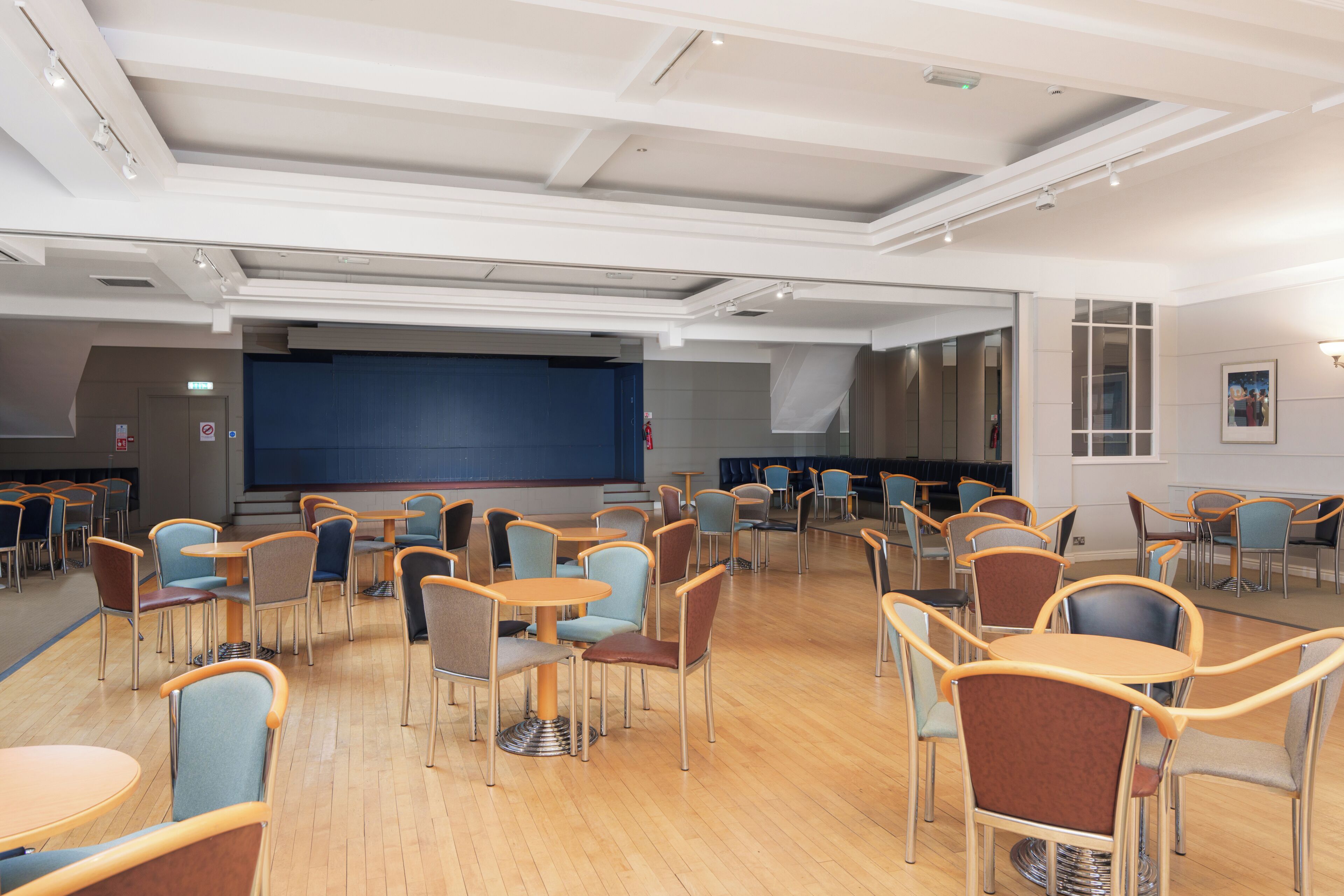 A spacious conference room with multiple tables and chairs, a large screen, and a stage area.