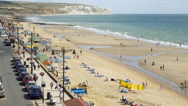 A coastal beach scene with a promenade lined with parked cars and beach umbrellas. - Trouville Hotel by Compass Hospitality (Sandown)