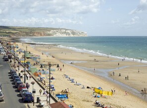 A coastal beach scene with a promenade lined with parked cars and beach umbrellas. - Trouville Hotel by Compass Hospitality (Sandown)