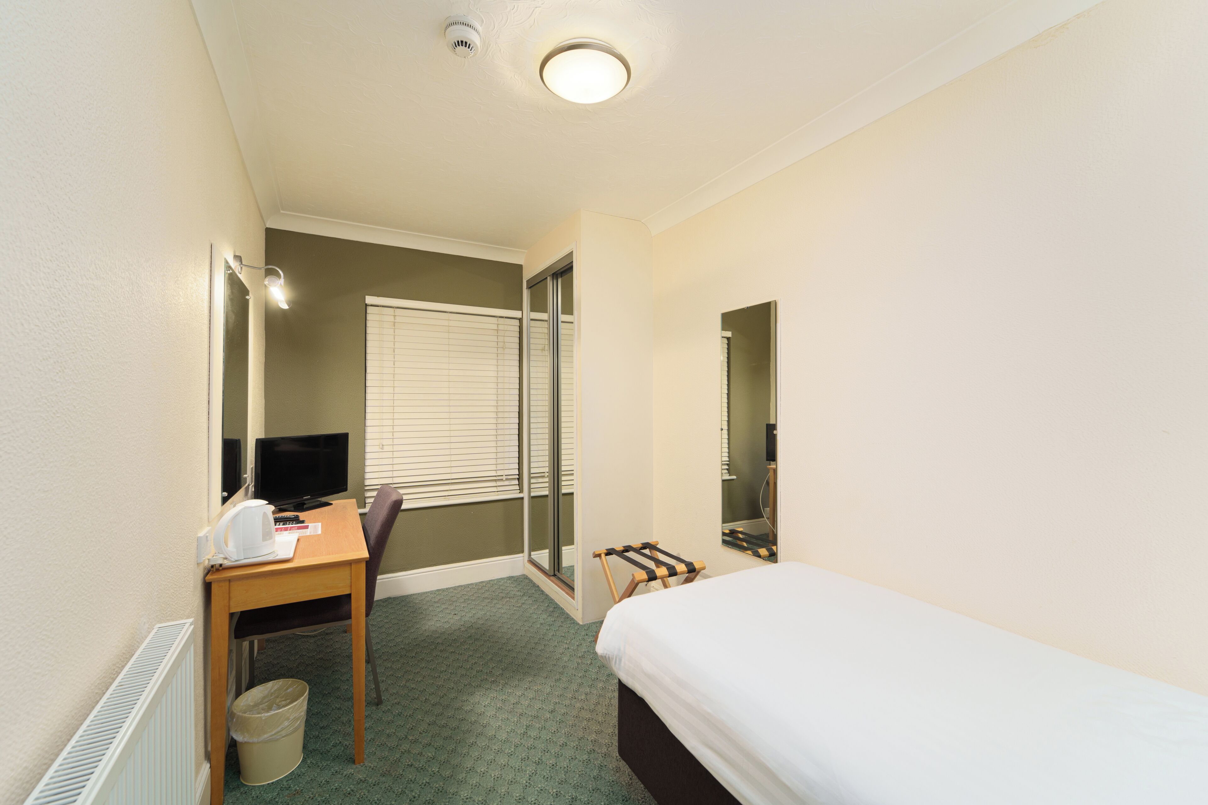 Ein Hotelzimmer mit Bett, Schreibtisch mit Computer, Stuhl, kleinem Tisch, Mülleimer und Duschbereich.