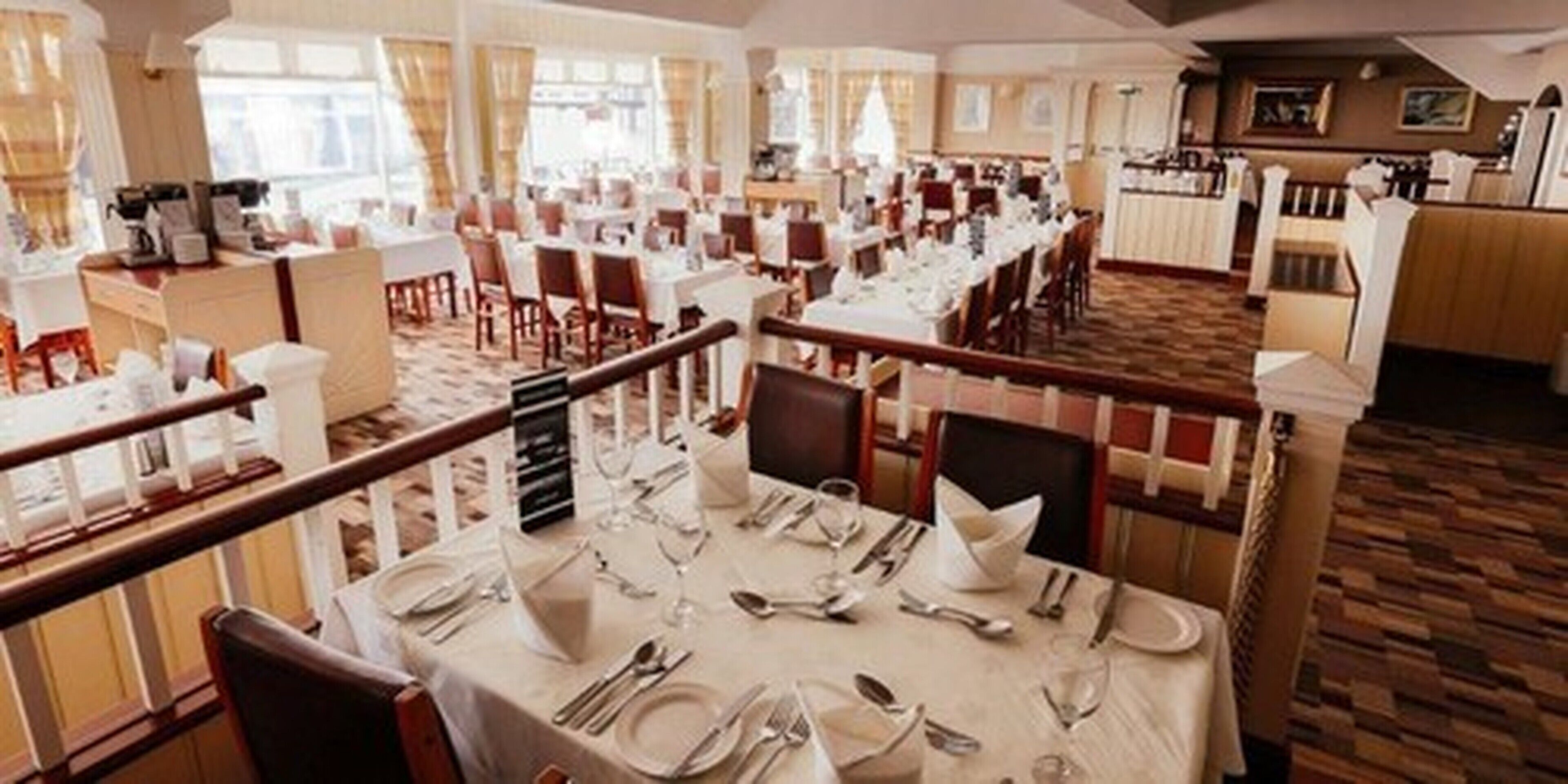 A spacious dining area with multiple tables set for service, high ceilings, and large windows allowing natural light.