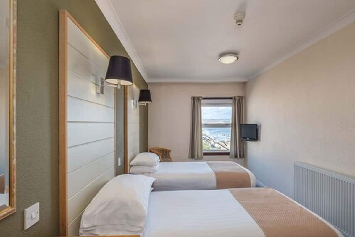 A hotel room with two beds, a window with a view, a television, and a lamp.