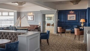 A hotel lobby with a grand staircase, a seating area with a tufted sofa and armchairs, and a dark blue accent wall with framed artwork. - Trouville Hotel by Compass Hospitality (Sandown)