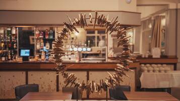 Interior de restaurante con una escultura de madera como pieza central, una zona de bar con botellas y una mesa de comedor con sillas.