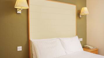 A hotel room with a large bed, two bedside lamps, a wooden headboard, a nightstand with a telephone, and a wall socket.