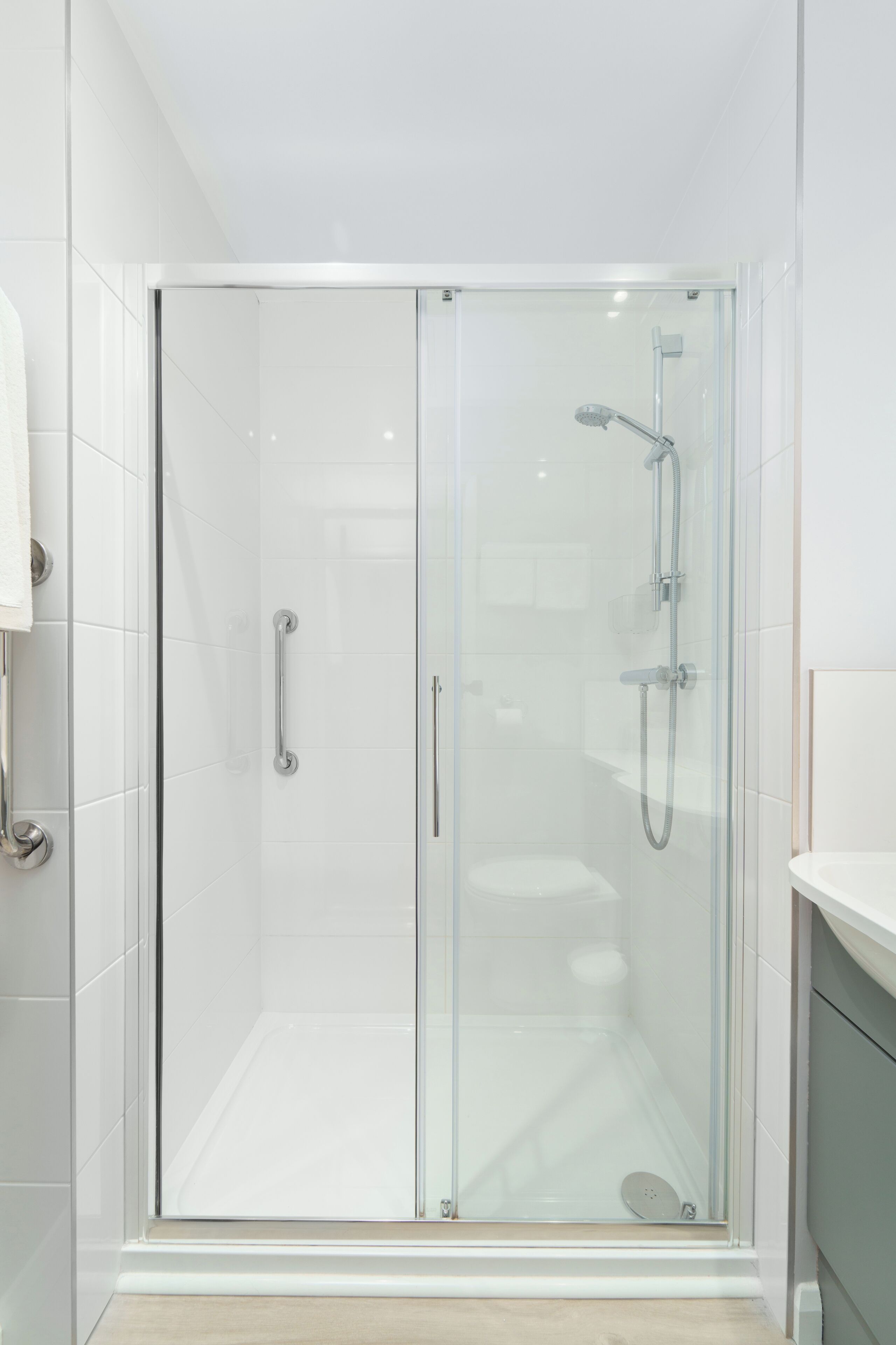 A modern bathroom with a glass-enclosed shower, white tiles, and a wooden floor.