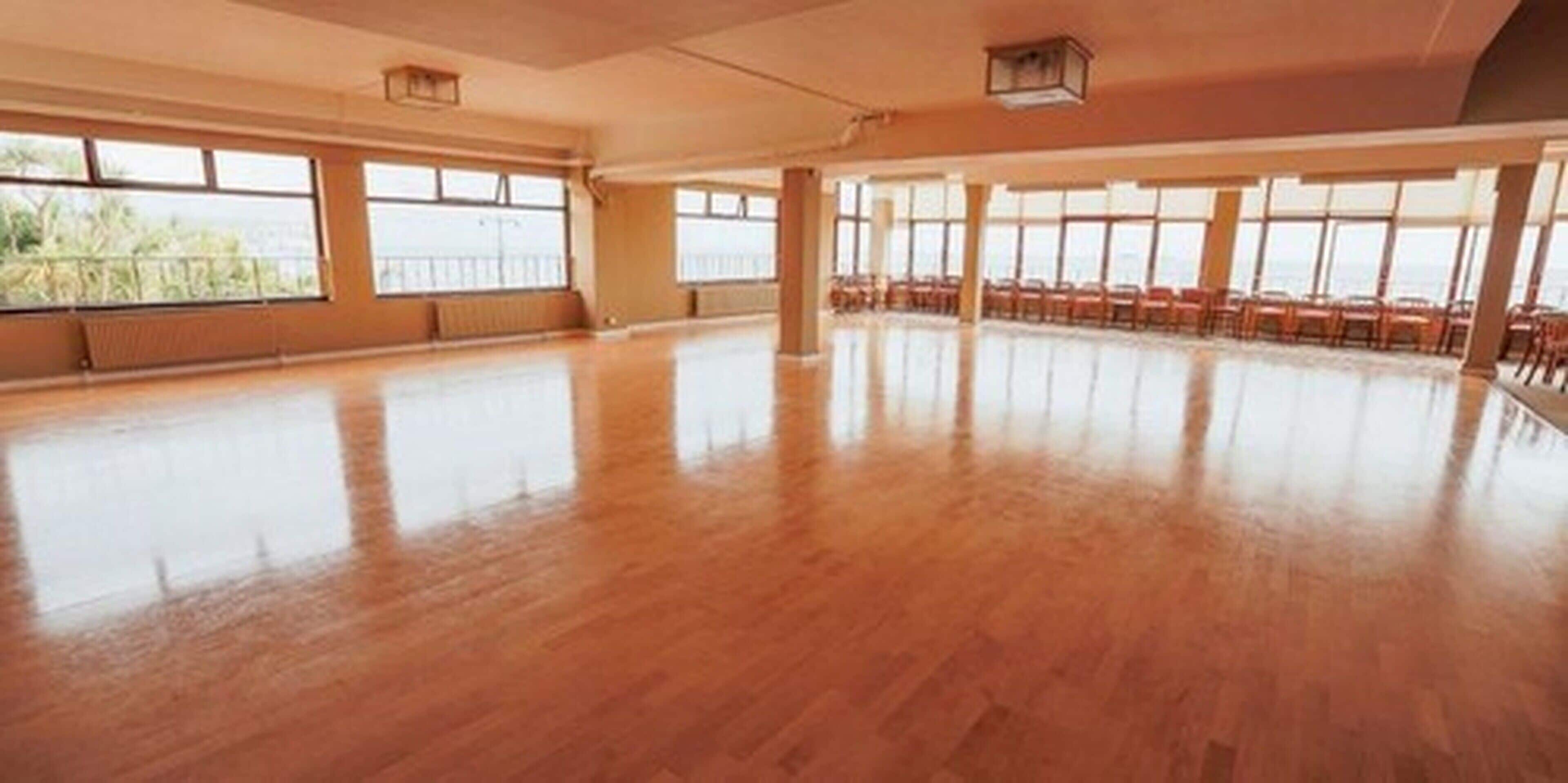 A spacious room with large windows, wooden flooring, and a high ceiling.