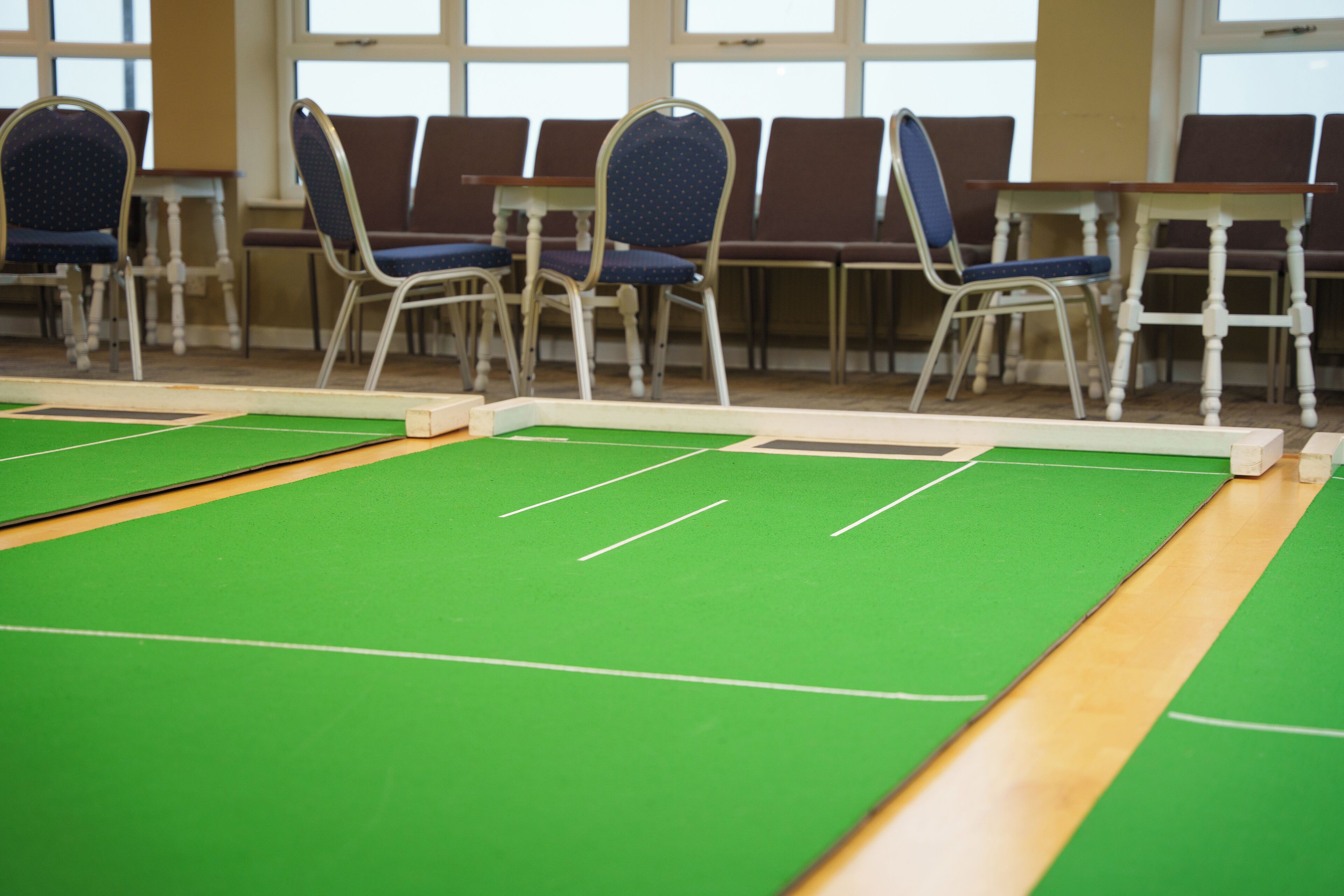 Eine Billardhalle mit grünen Tischen und Stuhlreihen.