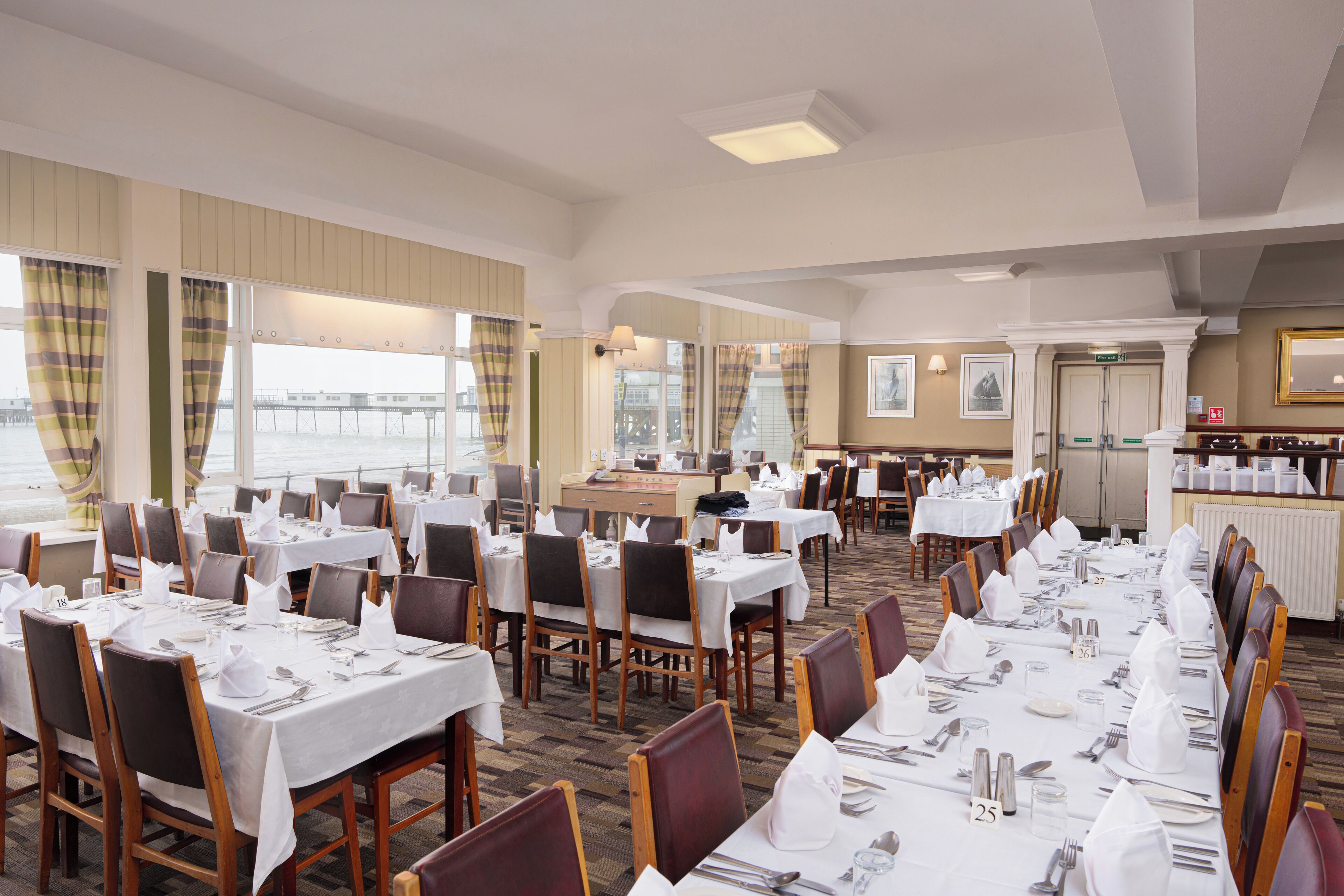 A large dining area with multiple tables set for service, a reception desk, and a view of the outside.