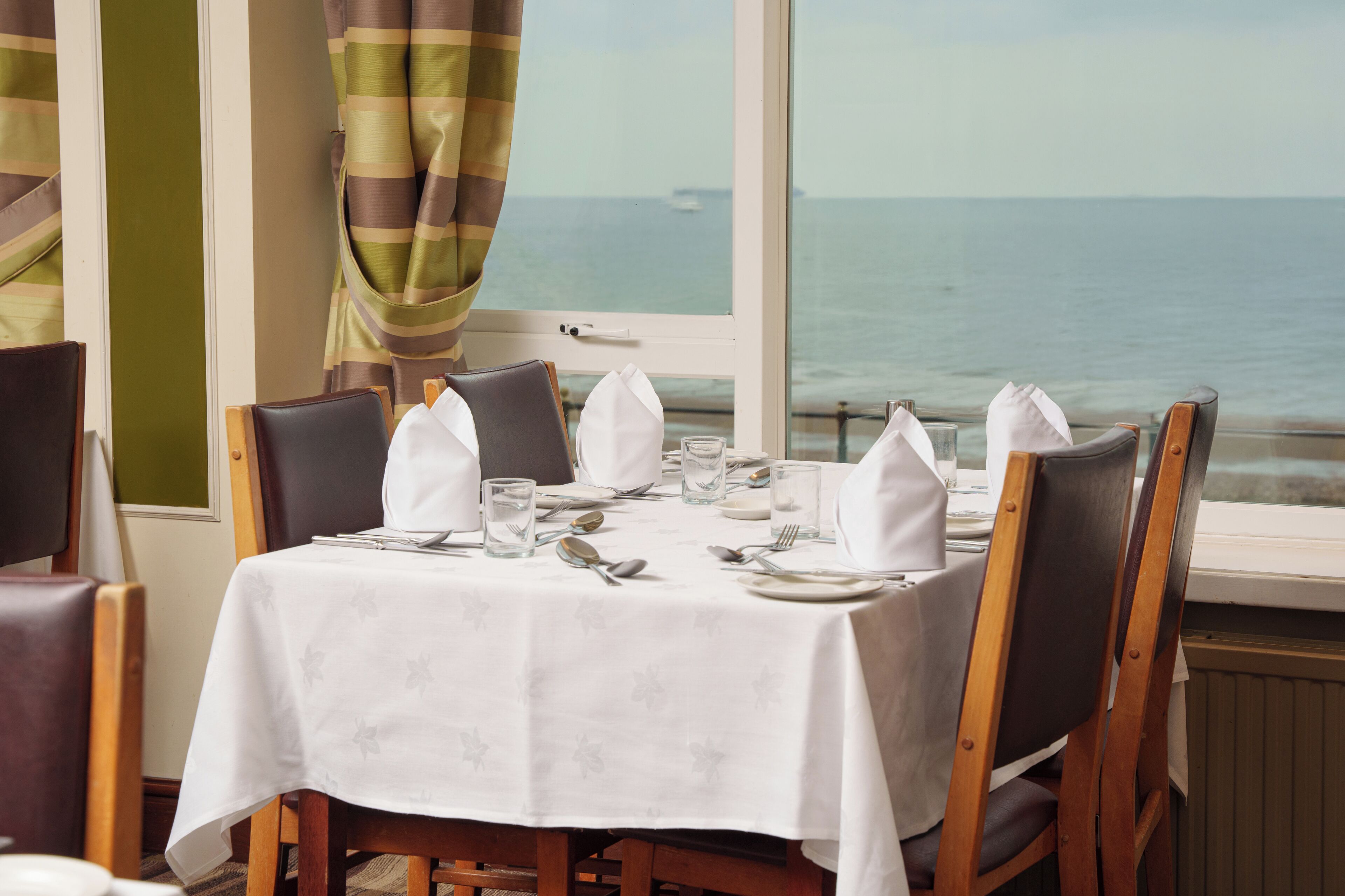 A dining table set for four with a view of the sea through a window.
