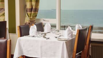 A dining table set for four with a view of the sea through a window.