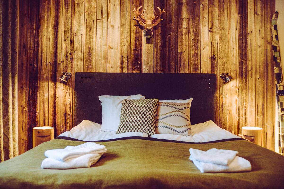 Ein Bett mit Holz-Kopfstück, zwei Kissen und zwei Nachttische mit Lampen.