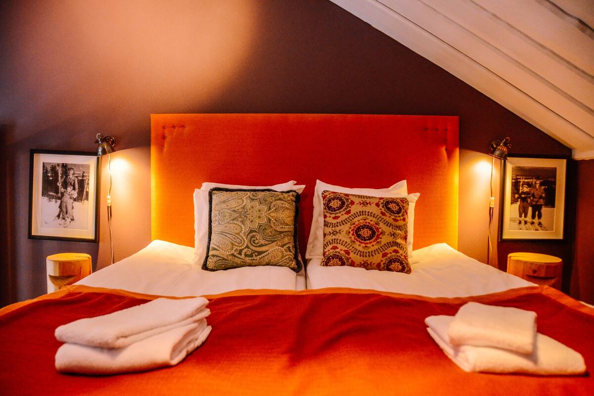 Ein Hotelzimmer mit rotem Kopfteil, zwei gemusterten Kissen, weißer Bettwäsche und zwei Nachttischlampen.