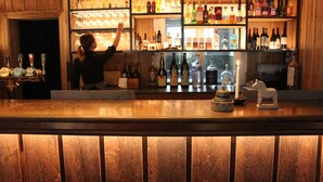 Un bar con estantes llenos de botellas y vasos, una barra de madera y una figura decorativa de un caballo.