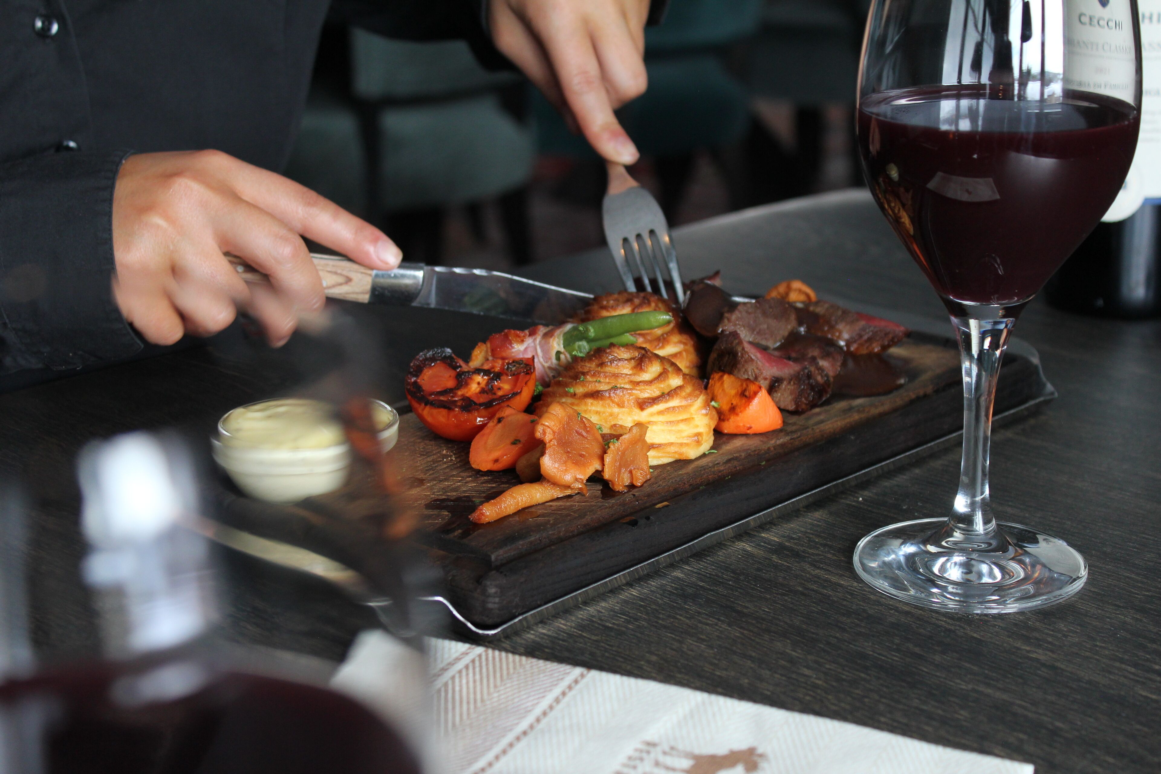 Una persona che cena con un piatto di cibo e un bicchiere di vino rosso su un tavolo.