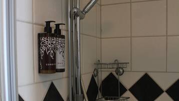 A shower with a handheld showerhead and a wall-mounted faucet. There are two bottles of hair conditioner on the wall.