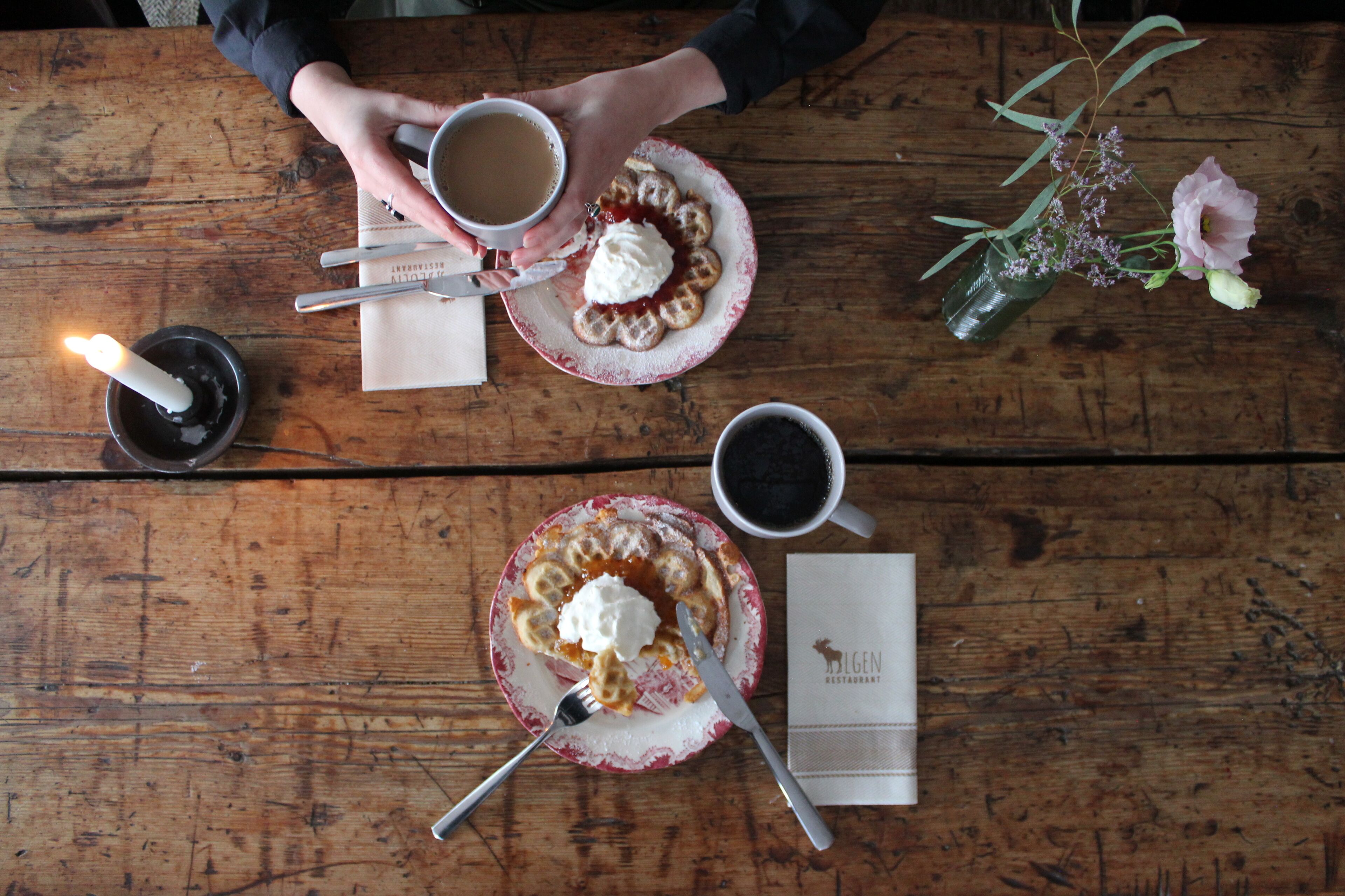 A wooden table with a plate of food, a cup of coffee, and a candle.