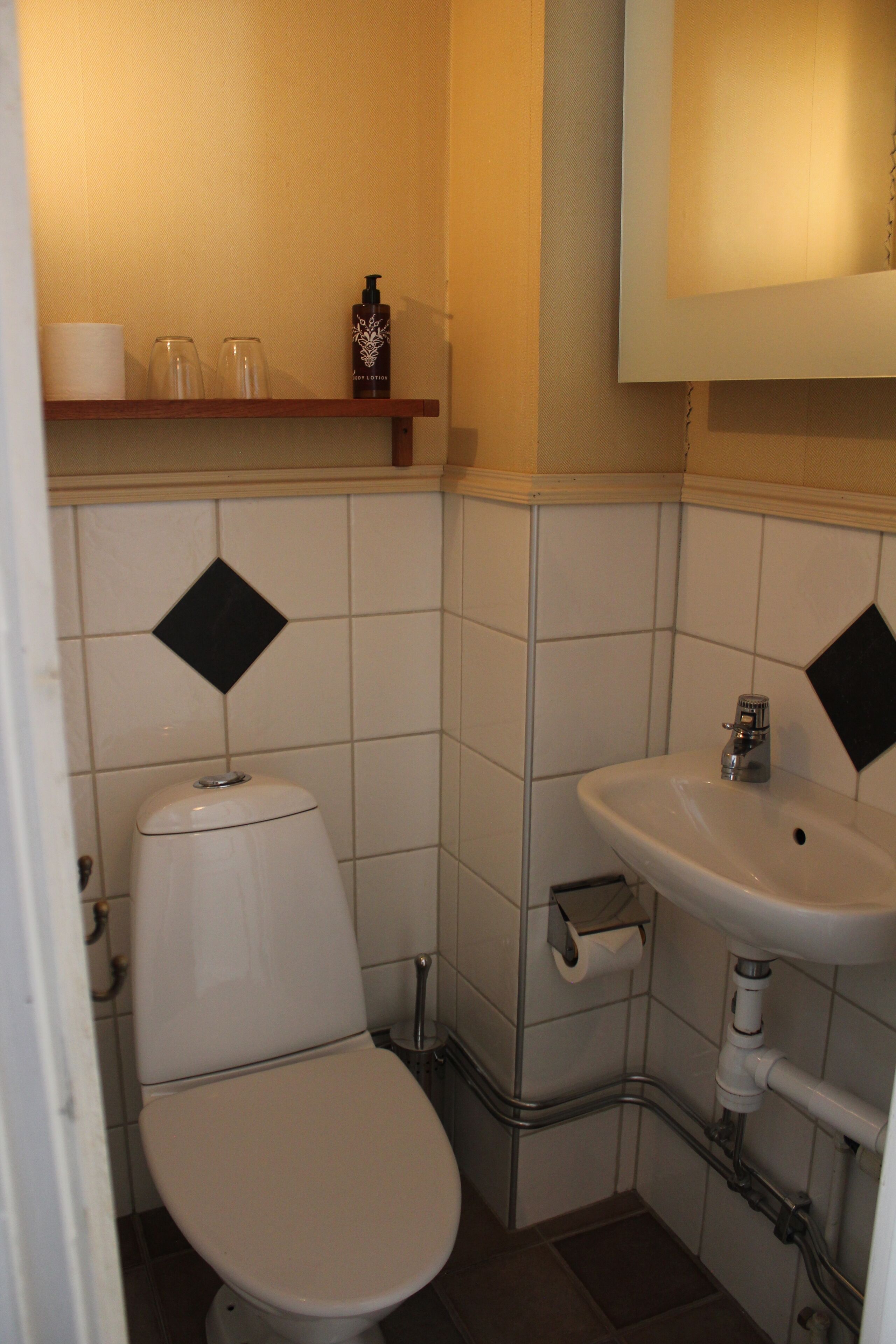 A small bathroom with a toilet, sink, and shelf with toiletries.