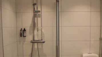 Una doccia con porta in vetro, un water e un piccolo ripiano con articoli da toilette.