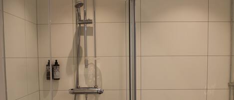 A shower with a glass door, a toilet, and a small shelf with toiletries.