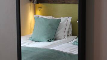 A room with a wooden headboard, a bed with white bedding and a teal pillow, and a bedside lamp.