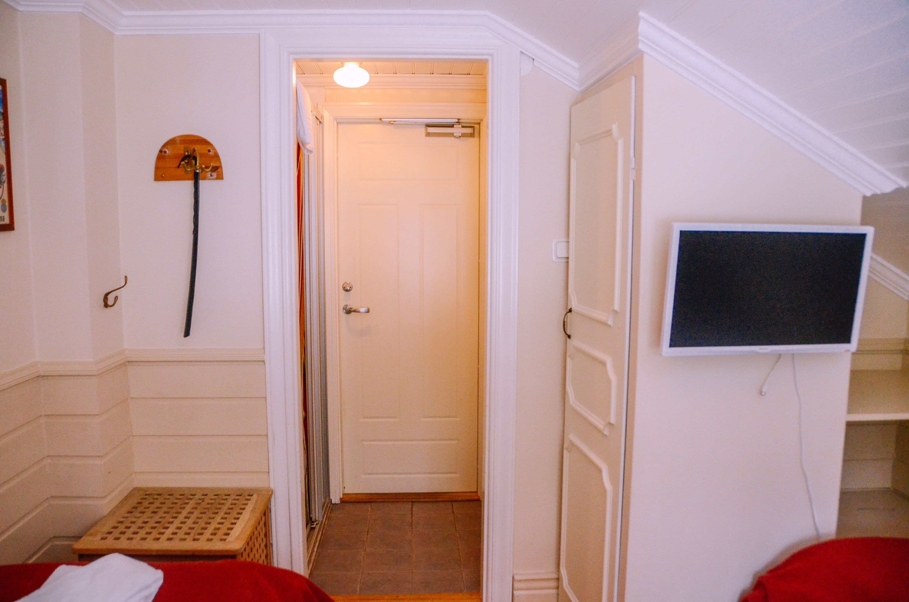 A hotel room with a bed, a small table, a TV mounted on the wall, and a door leading to another room.