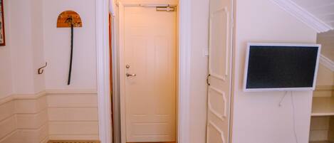 A hotel room with a bed, a small table, a TV mounted on the wall, and a door leading to another room.