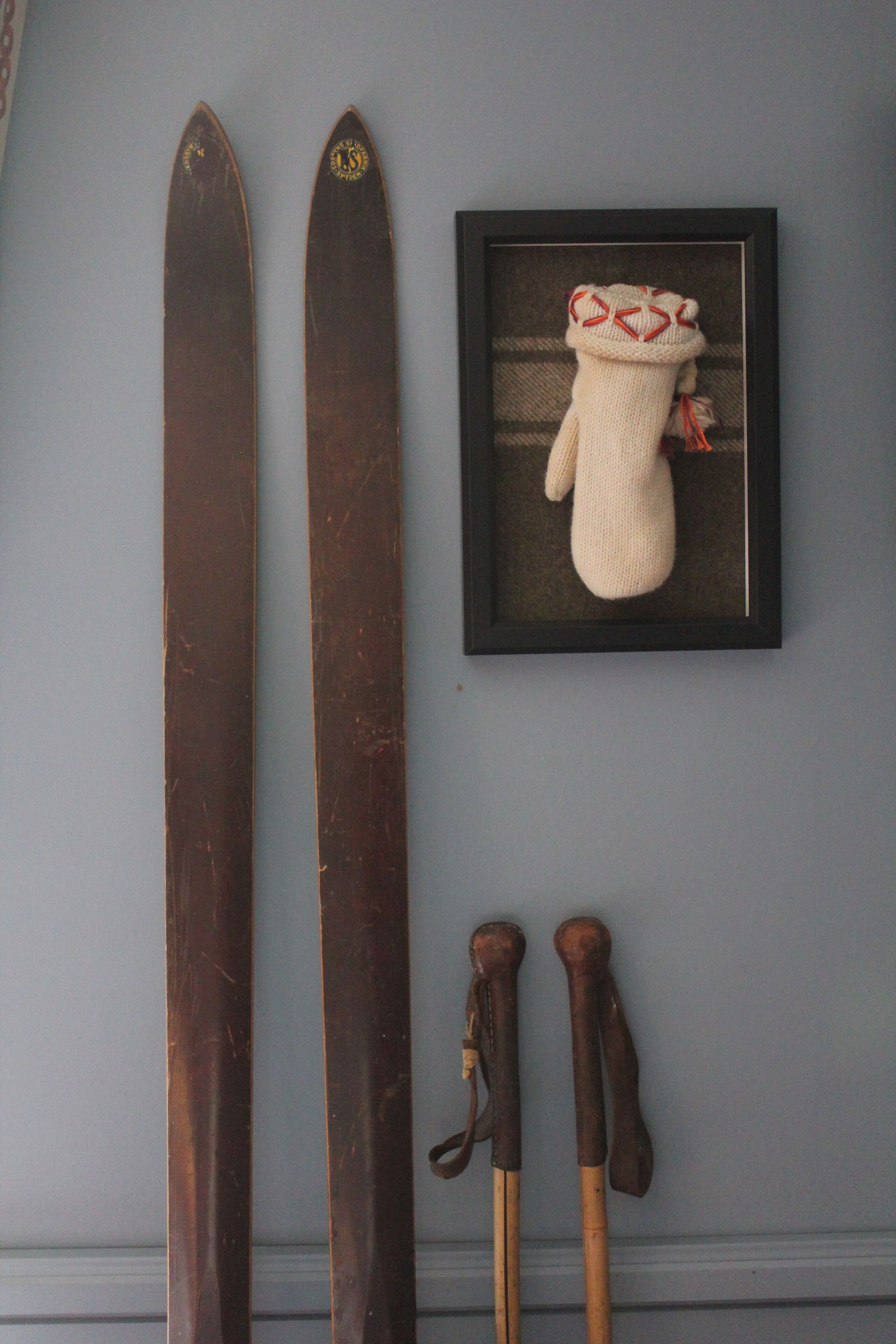Un par de esquíes, un par de bastones de esquí y un objeto tejido enmarcado en una pared.