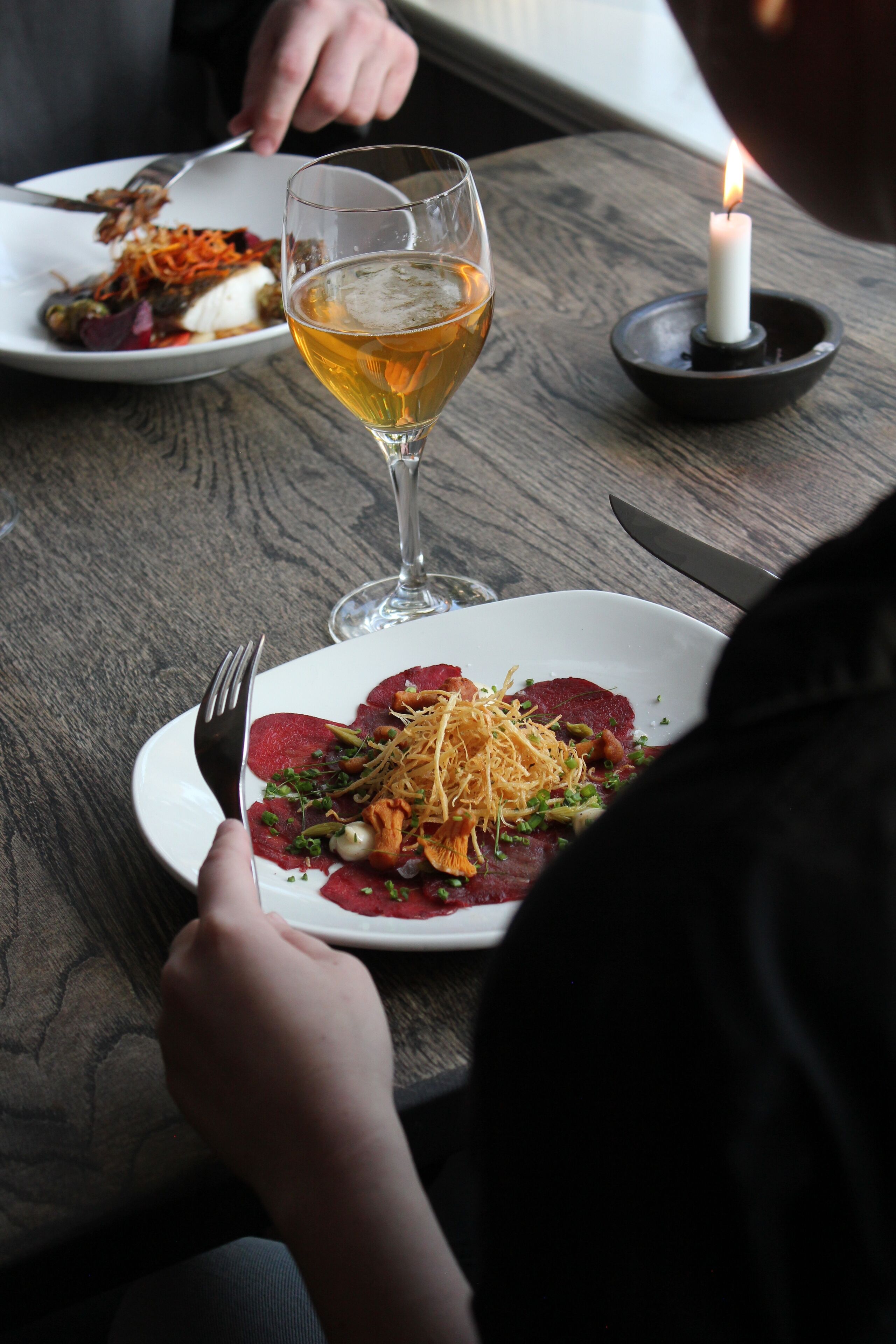 Una mesa de comedor con un plato de comida, una jarra de cerveza y una vela encendida.
