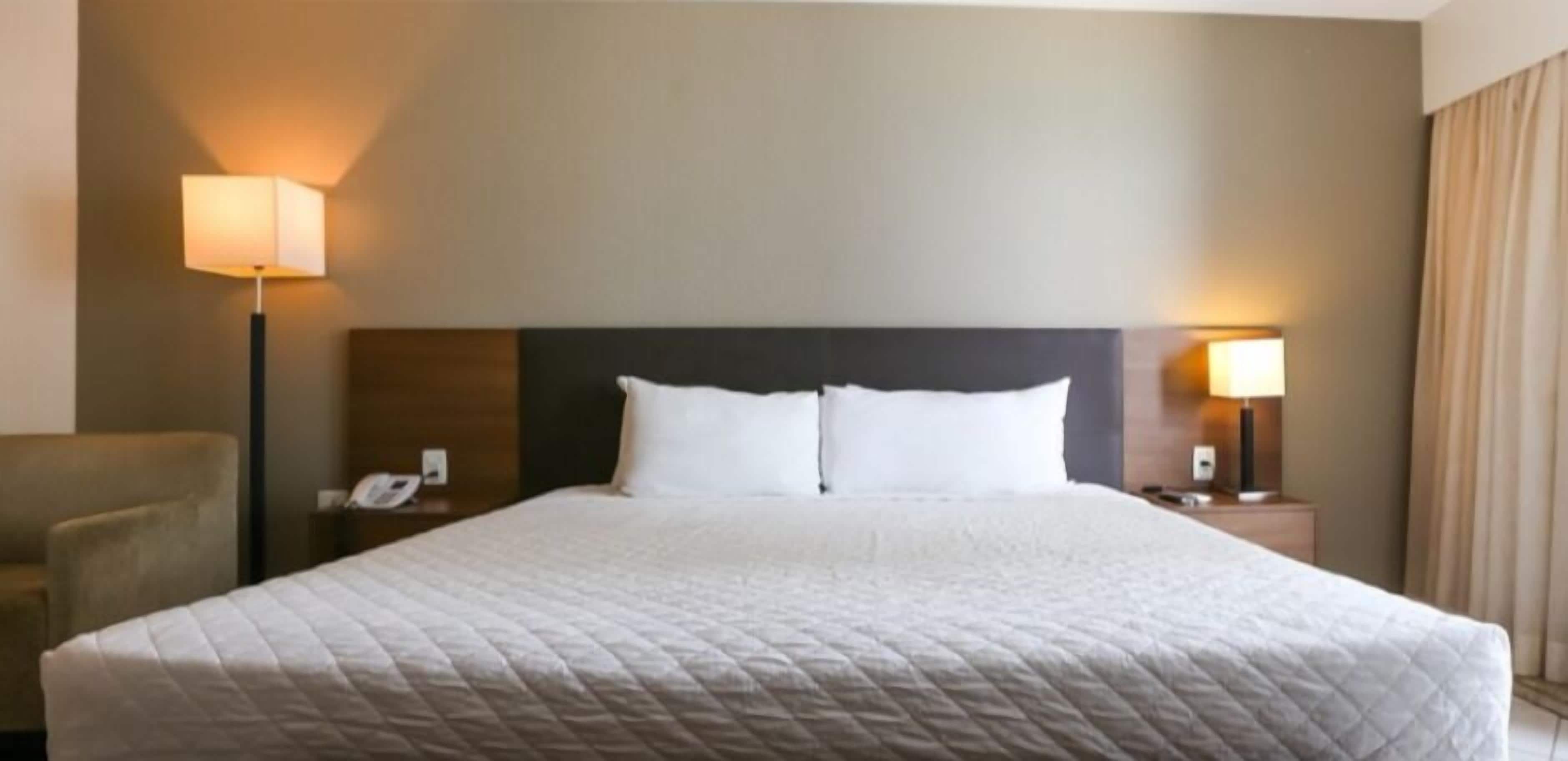 A hotel room with a large bed, two bedside tables with lamps, a chair, and a nightstand with a phone.