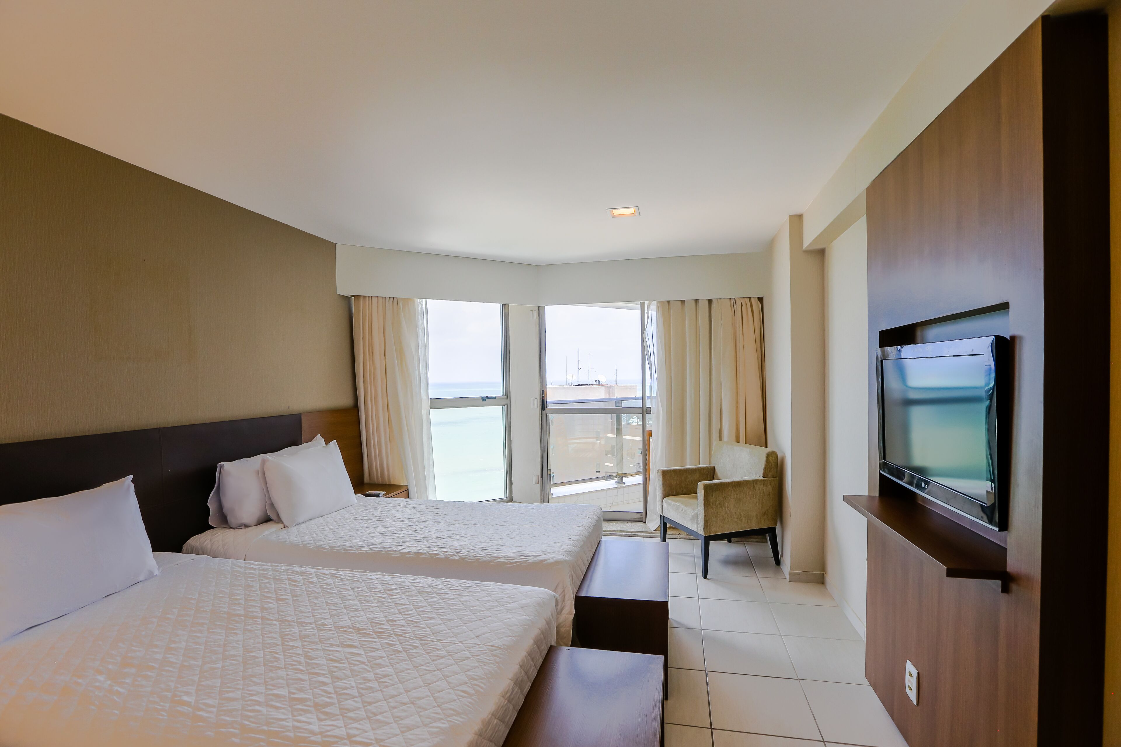 A hotel room with two beds, a TV, a chair, and a balcony with curtains.