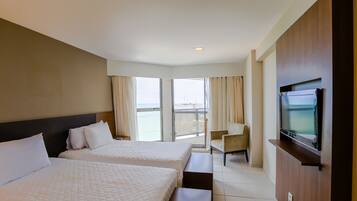 A hotel room with two beds, a TV, a chair, and a balcony with curtains.