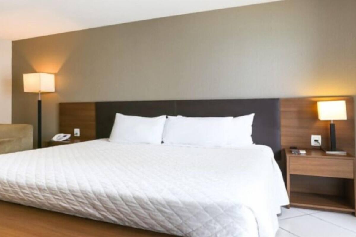 A hotel room with a large bed, two bedside tables, a chair, and two wall-mounted lamps.