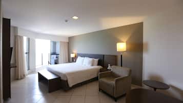 Una habitación de hotel con una cama grande, una mesita de noche, una silla, una pequeña mesa y una lámpara.