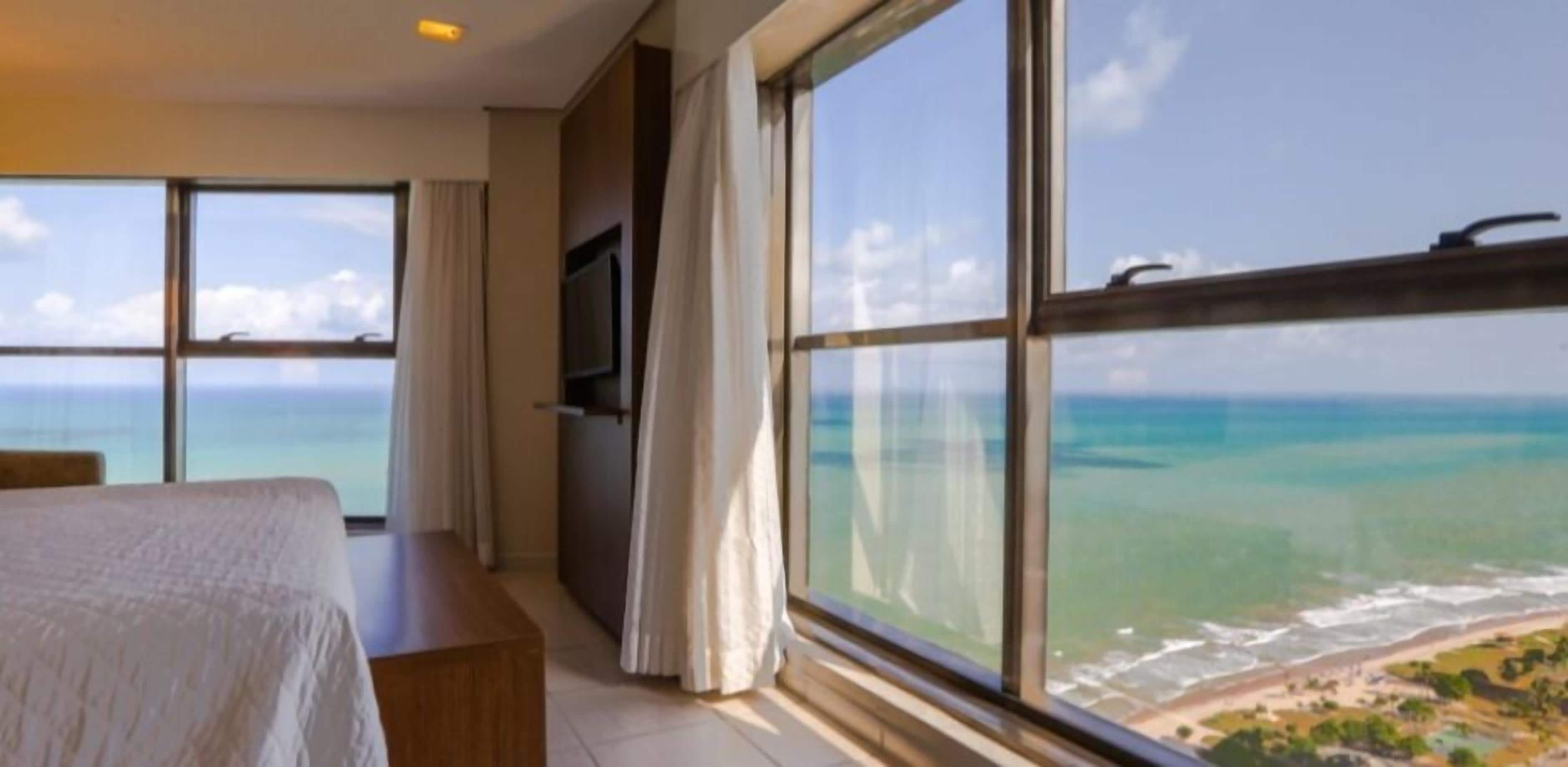 Habitación de hotel con un ventanal grande que ofrece vista al océano y la playa.