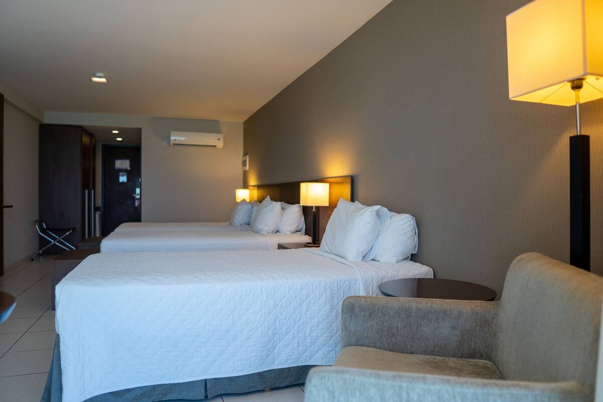 A hotel room with two beds, a sofa, a small table, and a lamp.