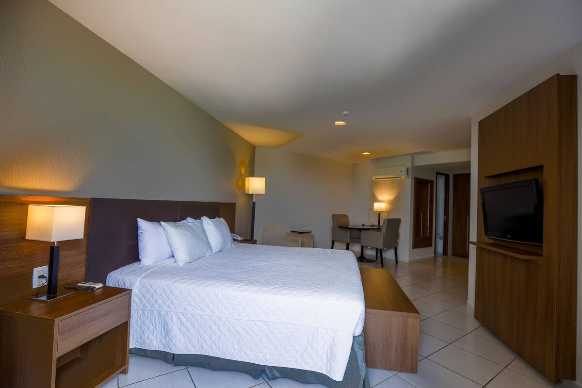 A hotel room with a large bed, bedside tables, a desk, and a TV.