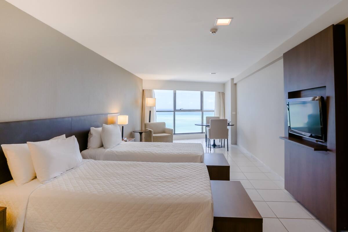 A hotel room with two beds, a TV, a desk, and a chair.